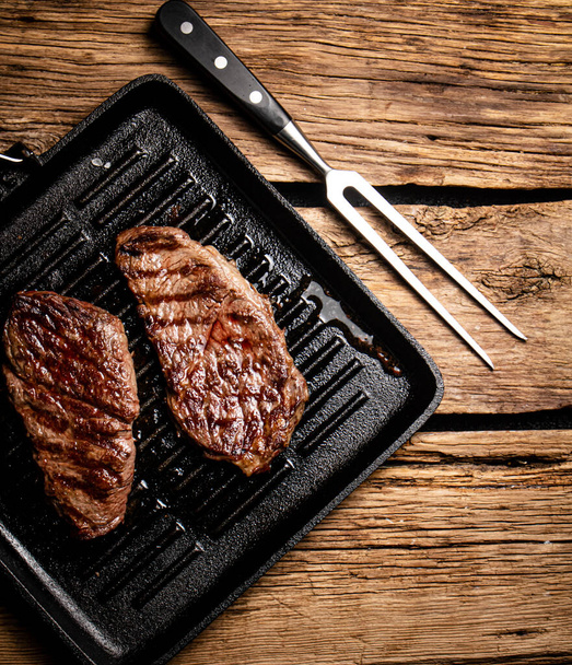 Grilled steak in a frying pan. On a wooden background. High quality photo - 写真・画像