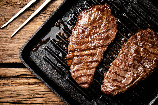 Grilled steak in a frying pan. On a wooden background. High quality photo - Фото, изображение