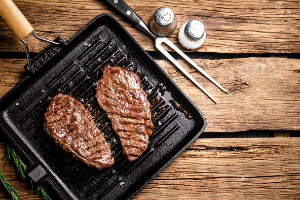 Grilled steak in a frying pan. On a wooden background. High quality photo - Foto, imagen