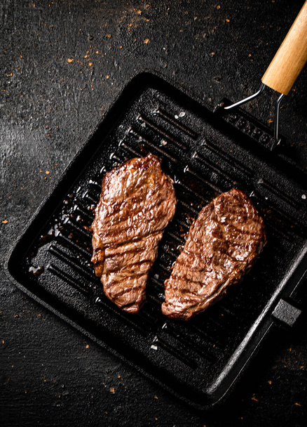 Delicious grilled steak in a frying pan. On a black background. High quality photo - Fotoğraf, Görsel