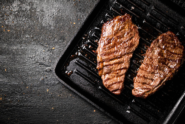 Delicious grilled steak in a frying pan. On a black background. High quality photo - 写真・画像