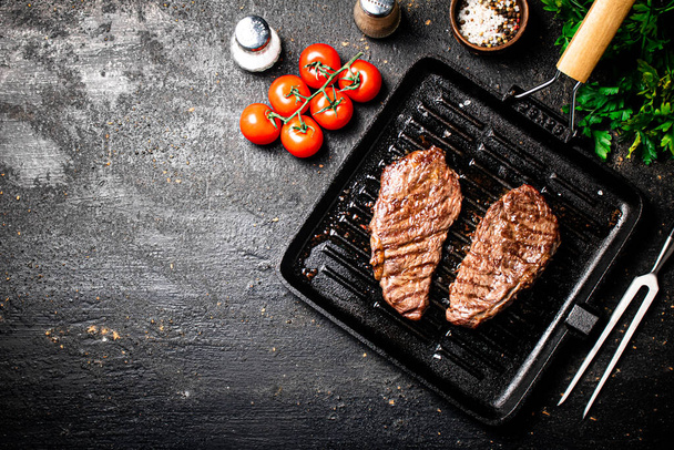 Grilled steak in a frying pan with tomatoes and spices. On a black background. High quality photo - Φωτογραφία, εικόνα