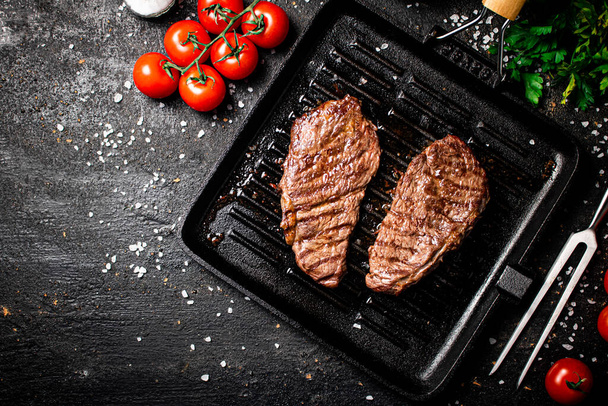 Grilled steak in a frying pan with tomatoes and spices. On a black background. High quality photo - Φωτογραφία, εικόνα