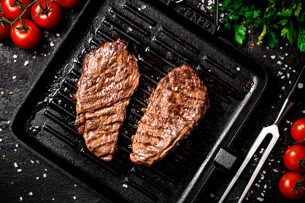 Grilled steak in a frying pan with tomatoes and spices. On a black background. High quality photo - Foto, imagen