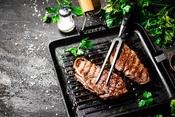 Grilled steak with parsley in a frying pan. On a black background. High quality photo - 写真・画像