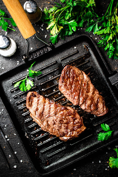 Grilled steak with parsley in a frying pan. On a black background. High quality photo - Foto, imagen