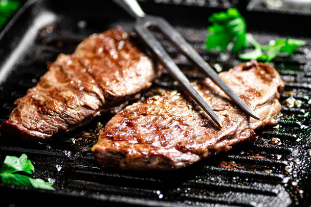 Grilled steak with parsley in a frying pan. On a black background. High quality photo - Foto, afbeelding