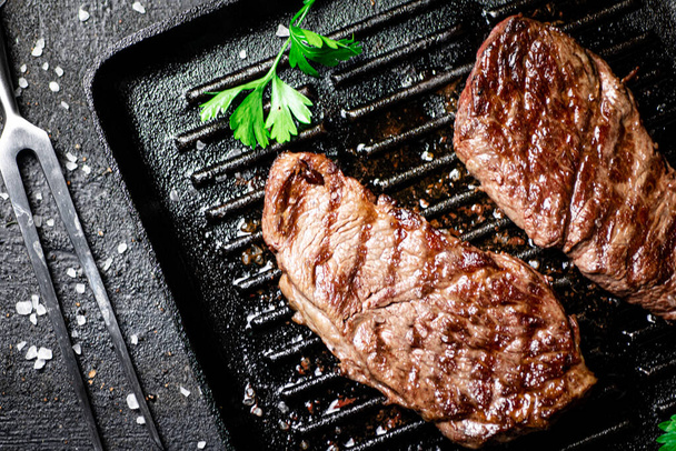 Grilled steak with parsley in a frying pan. On a black background. High quality photo - Φωτογραφία, εικόνα