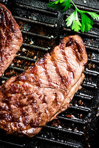 Grilled steak with parsley in a frying pan. On a black background. High quality photo - Foto, immagini