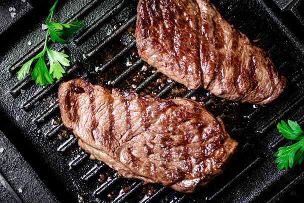 Grilled steak with parsley in a frying pan. On a black background. High quality photo - Photo, image
