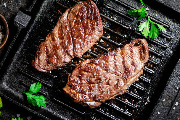 Grilled steak with parsley in a frying pan. On a black background. High quality photo - Фото, зображення