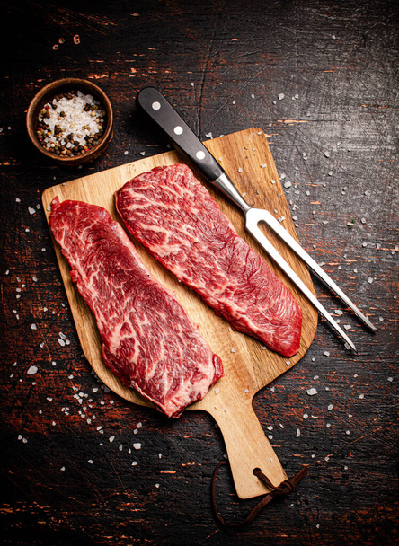 Raw steak on a wooden cutting board with spices. On a rustic dark background. High quality photo - Foto, afbeelding