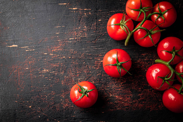 Fresh fragrant tomatoes on a branch. Against a dark background. High quality photo - Фото, изображение