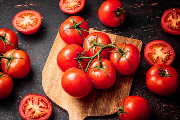 Fresh tomatoes on a wooden cutting board. Against a dark background. High quality photo - Fotografie, Obrázek