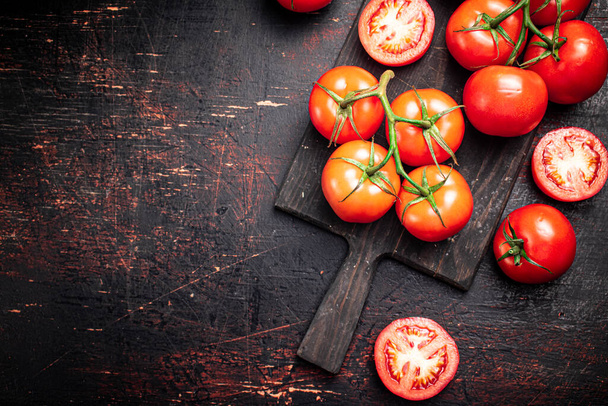 Fresh tomatoes on a wooden cutting board. Against a dark background. High quality photo - Fotoğraf, Görsel