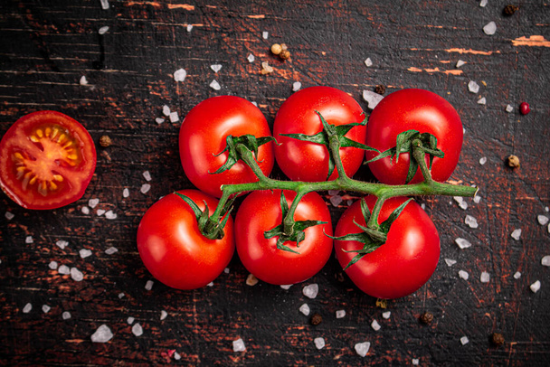 A branch of fresh tomatoes with pieces of salt. Against a dark background. High quality photo - Foto, Imagen