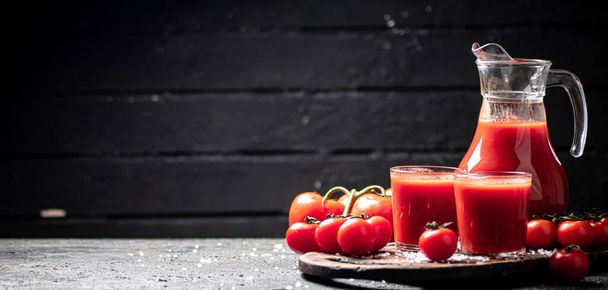 Glasses of tomato juice on a cutting board. On a black background. High quality photo - Photo, Image
