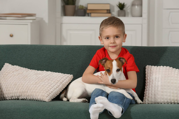 Μικρό αγόρι με το χαριτωμένο σκυλί του στον καναπέ στο σπίτι, χώρος για μήνυμα. Αξιαγάπητο κατοικίδιο - Φωτογραφία, εικόνα