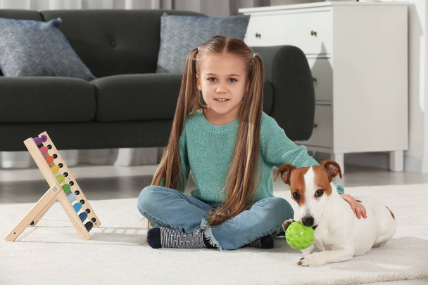 かわいい女の子が家の床で犬と遊んでいる。愛らしいペット - 写真・画像