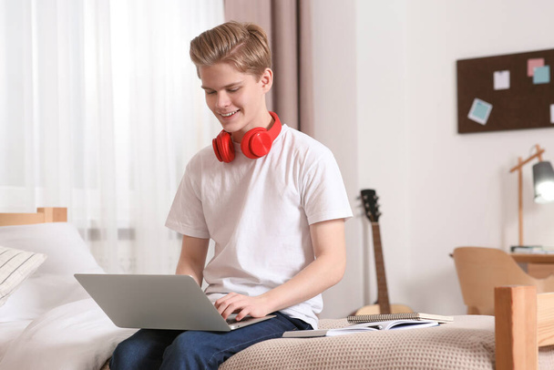Online learning. Smiling teenage boy typing on laptop at home - Фото, зображення