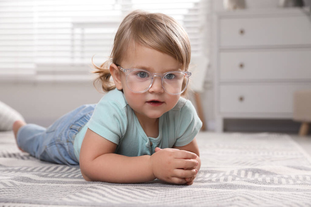 Cute little girl in glasses on floor at home. Space for text - Foto, imagen