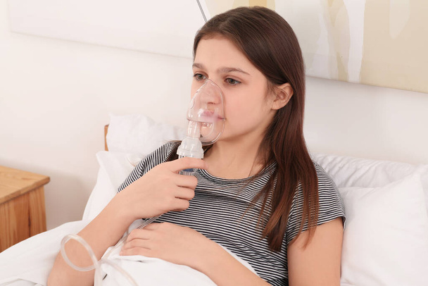 Cute girl using nebulizer for inhalation on bed at home - Fotó, kép