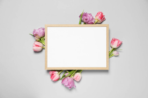 Empty photo frame and beautiful flowers on light gray background, top view. Space for design - Valokuva, kuva