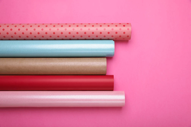 Rolls of colorful wrapping paper on pink background, flat lay - Фото, изображение