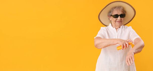 Mujer mayor que aplica crema protector solar sobre la piel sobre fondo amarillo con espacio para el texto - Foto, Imagen