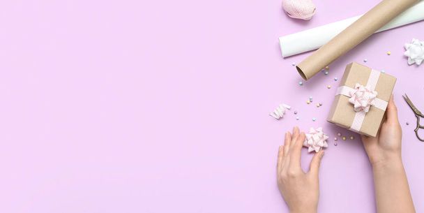 Mani femminili con confezione regalo, fiocchi e carta da regalo su sfondo lilla con spazio per testo, vista dall'alto - Foto, immagini