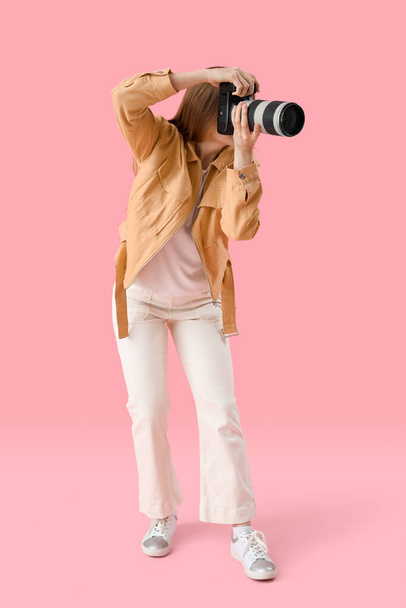 Young female photographer with professional camera on pink background - Foto, afbeelding