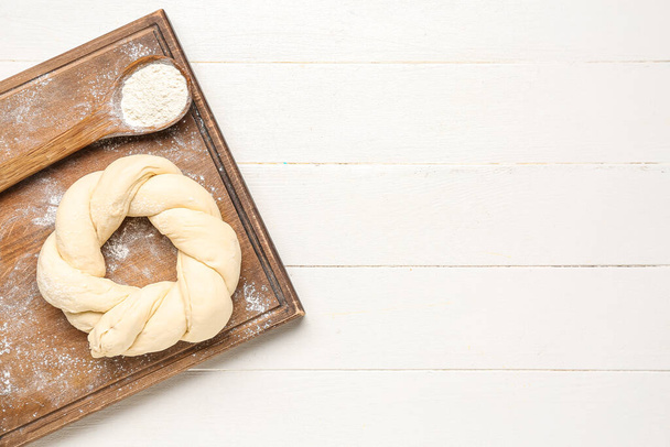 Bord met ongekookt Italiaans paasbrood en een lepel bloem op witte houten ondergrond - Foto, afbeelding