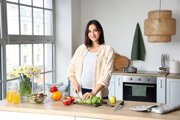 Молода вагітна жінка робить овочевий салат на кухні
 - Фото, зображення