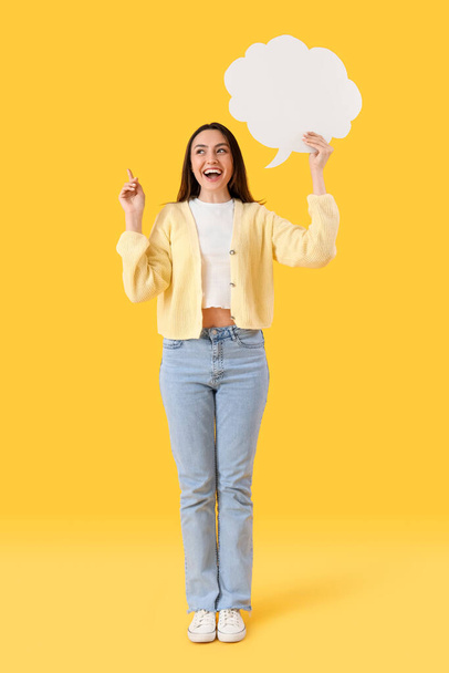 Young woman with blank speech bubble pointing at something on yellow background - Foto, afbeelding