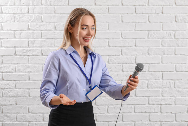 Γυναίκα δημοσιογράφος με μικρόφωνο σε λευκό φόντο τούβλο - Φωτογραφία, εικόνα
