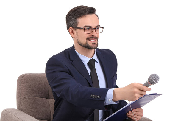 Male journalist with microphone and clipboard in armchair on white background - Foto, imagen