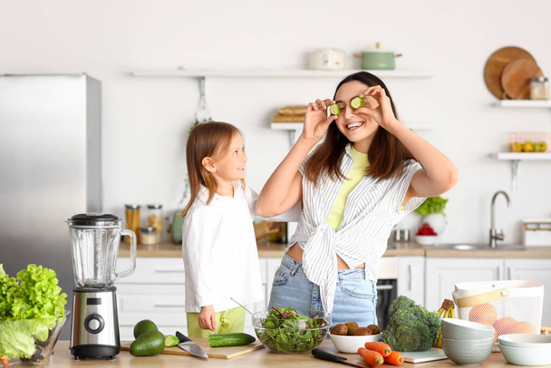 Bambina con la madre e fette di cetriolo divertirsi in cucina - Foto, immagini