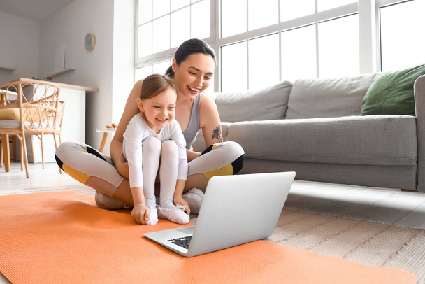 Sporty young woman and her little daughter training with laptop at home - Zdjęcie, obraz
