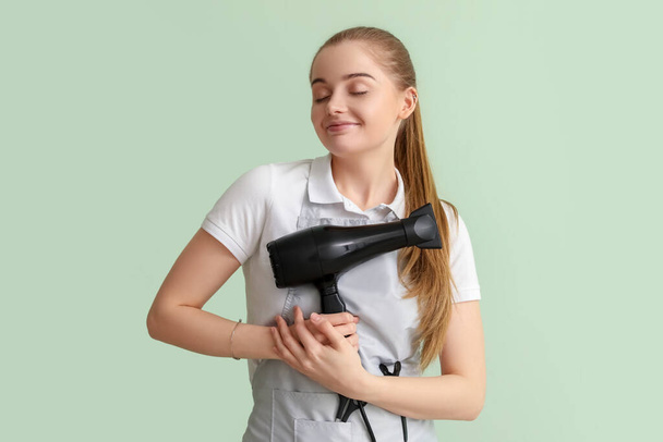 Female hairdresser with dryer on green background - Photo, Image