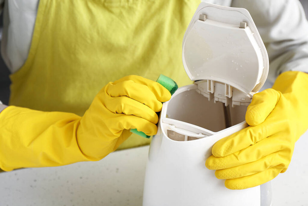 Nainen keltaisissa käsineissä puhdistamassa vedenkeitintä valkoisella pöydällä - Valokuva, kuva