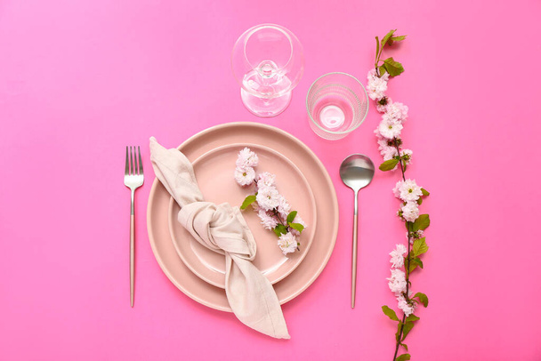 Beautiful table serving with cutlery, blooming tree branches and folded napkin on pink background - Foto, afbeelding