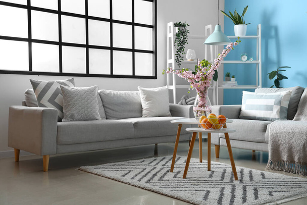 Інтер'єр стильної вітальні з сірими диванами і квітучими гілками сакури на кавовому столі
 - Фото, зображення