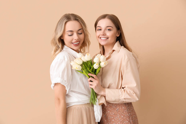 Jeunes sœurs avec tulipes sur fond beige - Photo, image