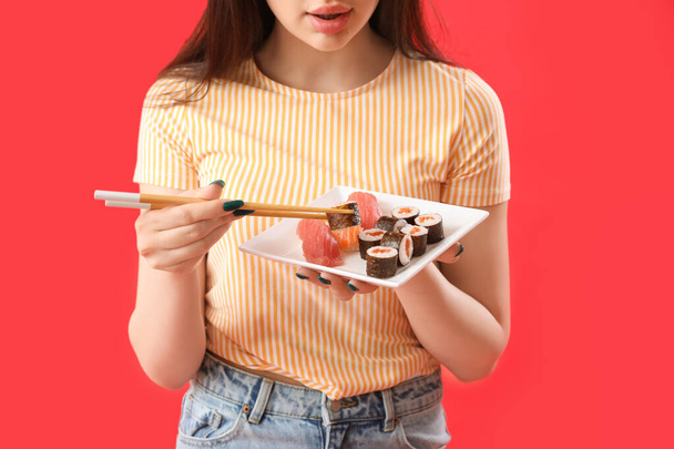 Jonge vrouw met sushi broodjes en stokjes op rode achtergrond, close-up - Foto, afbeelding