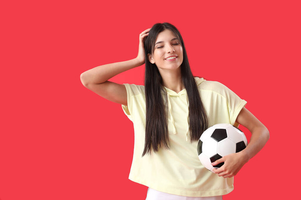Jonge vrouw met voetbal op rode achtergrond - Foto, afbeelding