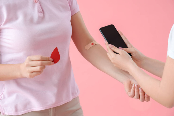 Mujer joven tomando foto de donante de sangre sobre fondo rosa, primer plano - Foto, imagen