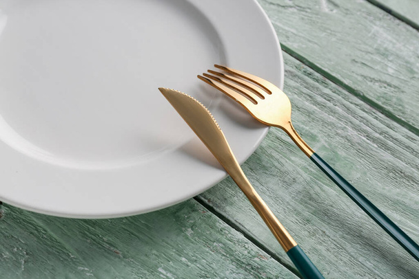 Couteau doré avec fourchette et assiette sur fond de bois vert - Photo, image