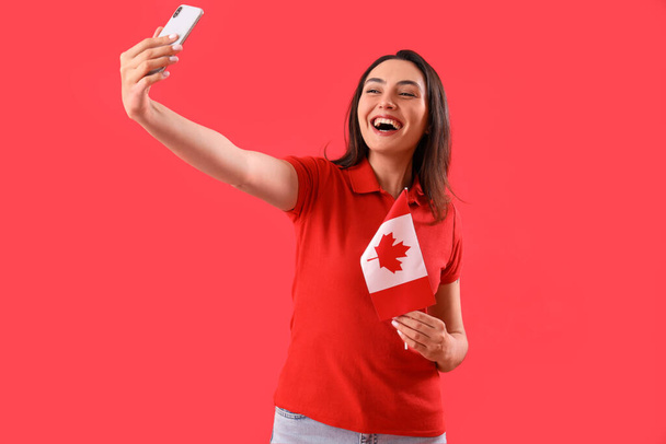 Молодая женщина с флагом Канады делает селфи на красном фоне - Фото, изображение