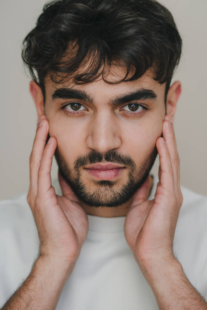 Close-up view of a handsome young man looking at camera expertising his face before shaving isoalted over grey background. Facial beauty. Facial skincare - Photo, Image