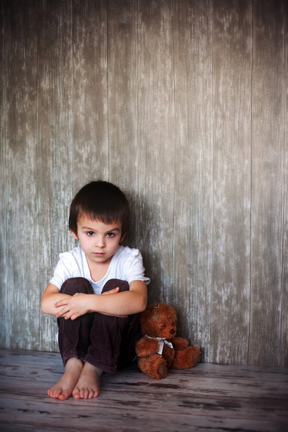 Young boy, sitting on the floor with his teddy bear, sad - 写真・画像